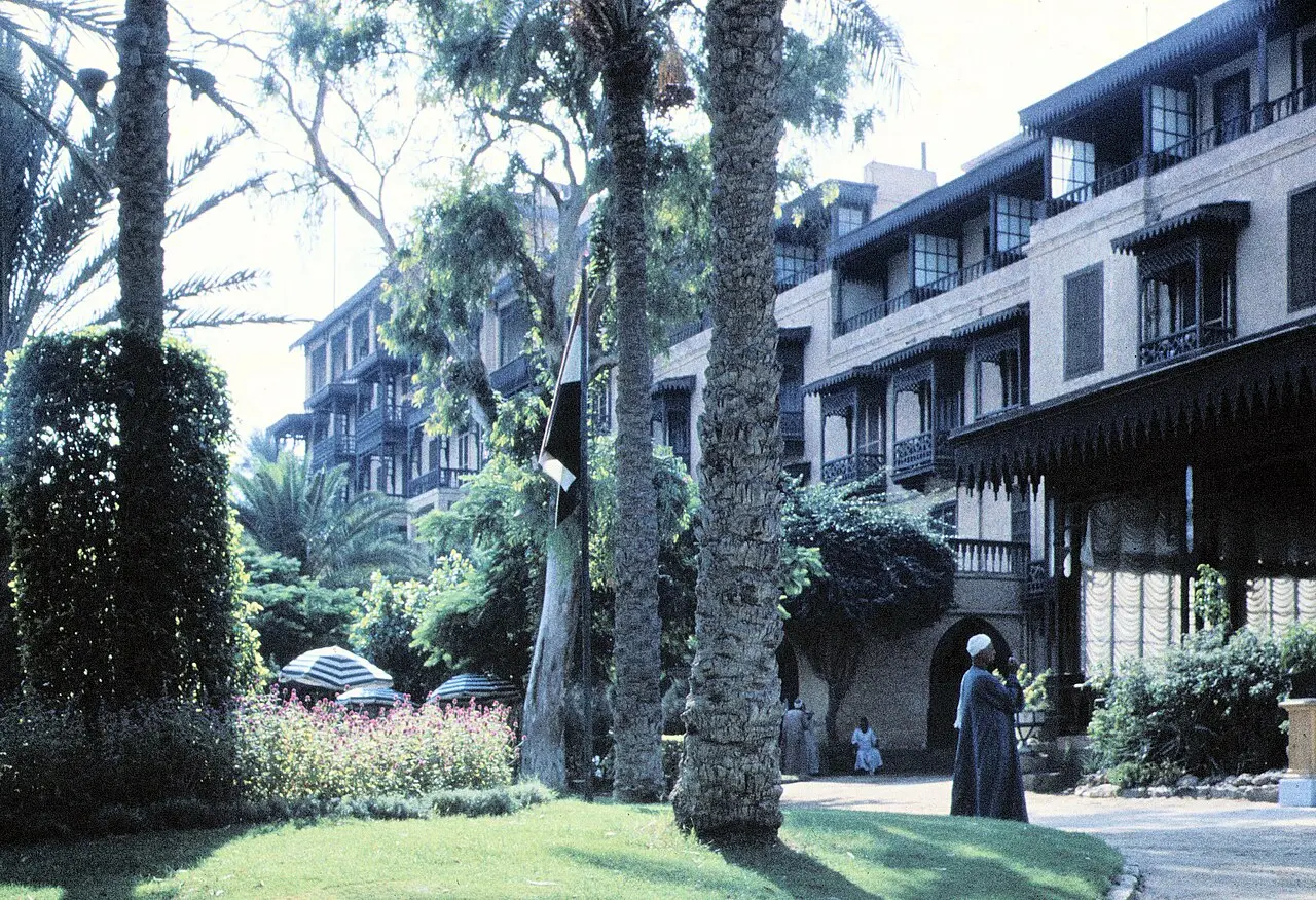 Mena House hotel wing with mashrabiya balconies behind tall palm trees in its garden
